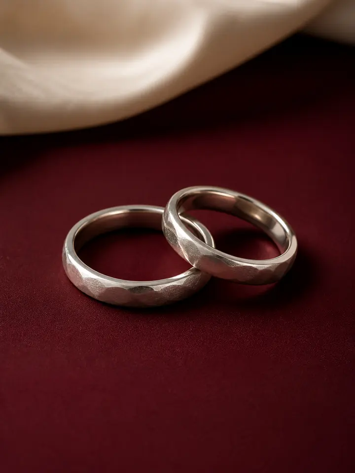 Sepasang cincin kawin perak di atas latar maroon dan kain cream